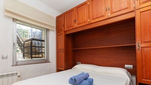Un dormitorio con cama, armario de madera y ventana con vistas a un edificio.