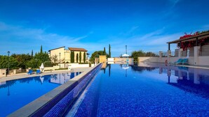 A swimming pool with clear blue water, surrounded by buildings and greenery. - Apartment Apj03 - Anesi (Kouklia)