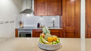 A kitchen with wooden cabinets, a stainless steel range hood, a microwave, and a fruit bowl on the counter.