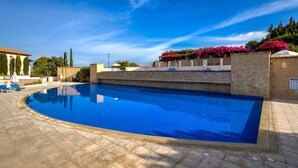 A swimming pool with a curved edge, surrounded by lounge chairs and a stone wall. - Apartment Apj03 - Anesi (Kouklia)