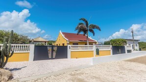 A residential property with a gated entrance, a red-roofed house, and a palm tree. - NEW Casa Kudawecha (Noord)