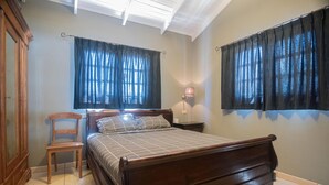 A bedroom with a wooden bed, a chair, two nightstands, and a wall-mounted lamp. - NEW Casa Kudawecha (Noord)