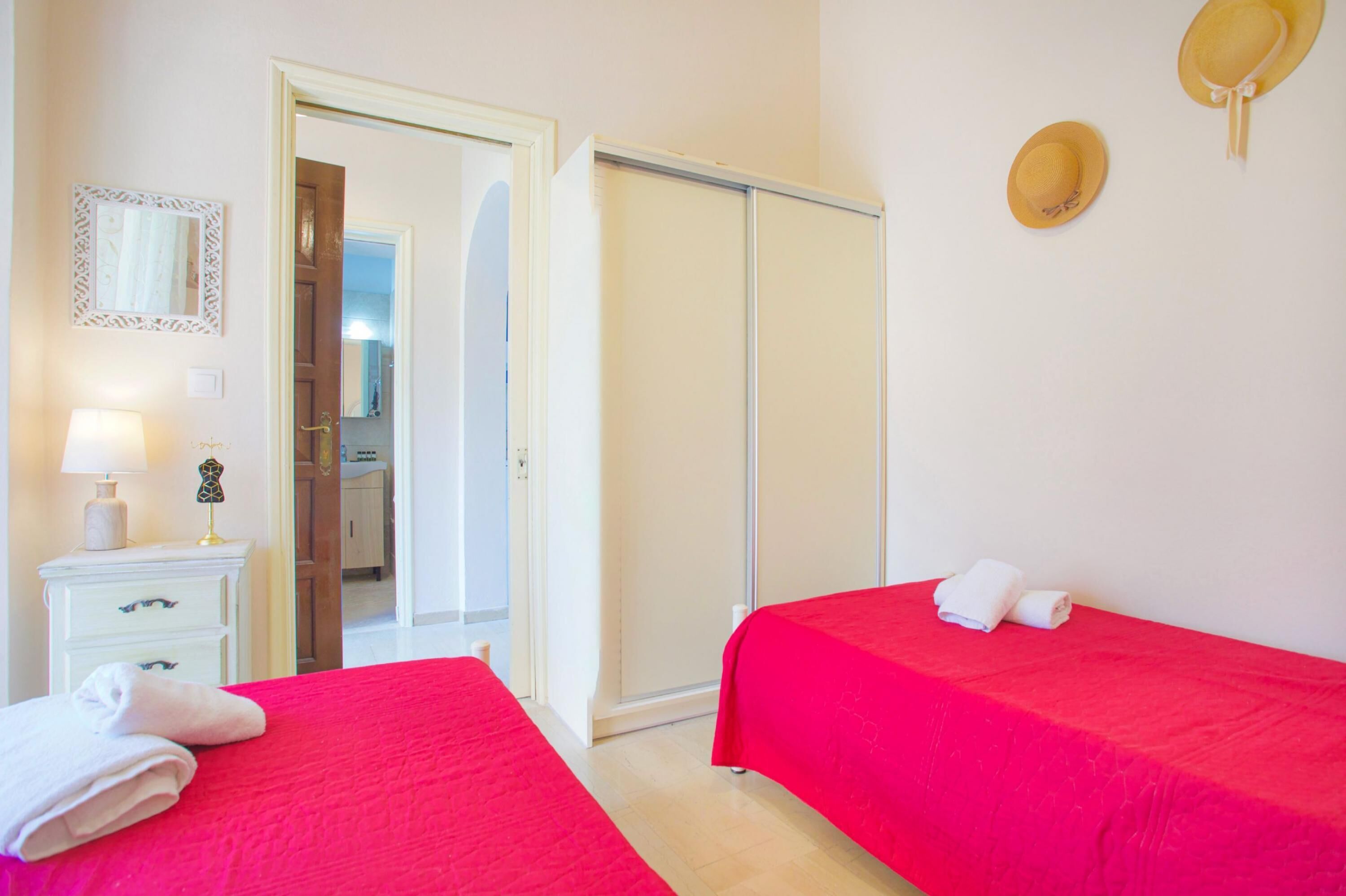 Quarto de hotel com duas camas, um guarda-roupa, um espelho e um chapéu na parede.