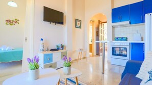 A modern kitchen with blue cabinets, a built-in oven, and a refrigerator. There is a dining area with a round table and two potted plants.