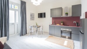 Une cuisine moderne avec des meubles gris, un réfrigérateur en acier inoxydable et un coin repas comprenant une table et des chaises.