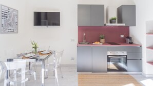 Une cuisine moderne dotée d’un four encastré, d’un coin repas avec des chaises transparentes et d’un téléviseur à écran plat fixé au mur.