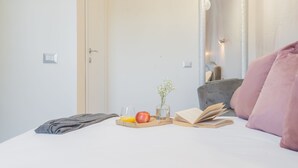 Une chambre à coucher avec un lit, une table de chevet sur laquelle se trouve un livre, un verre d’eau, une pomme et un vase rempli de fleurs.