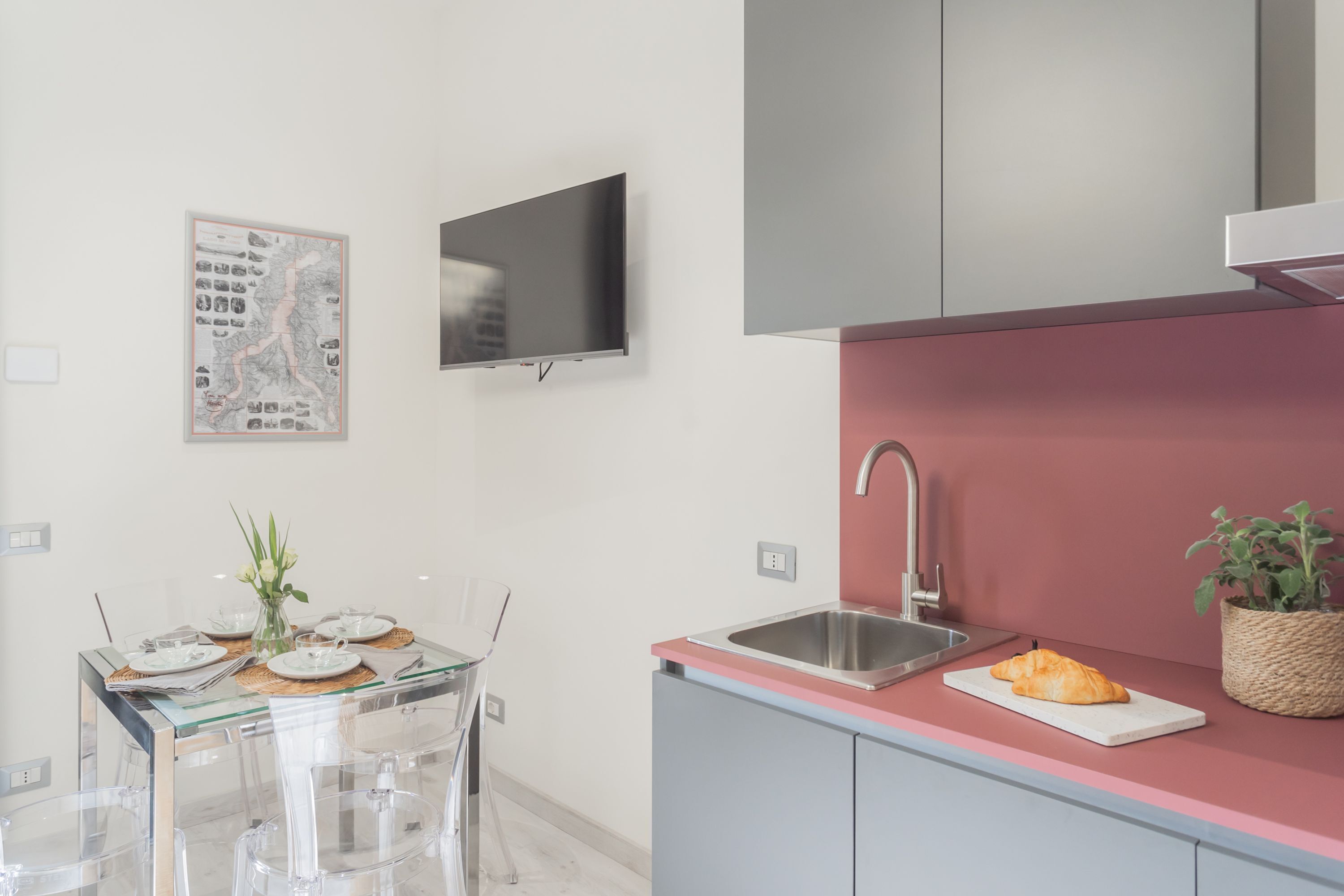 Eine moderne Küche mit einer rosa Arbeitsplatte, einem Edelstahl-Spülbecken und einem flachbildfernseher an der Wand.