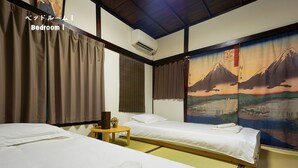 Una camera da letto tradizionale in stile giapponese con due letti, pavimento in tatami e un dipinto raffigurante un paesaggio montano.
