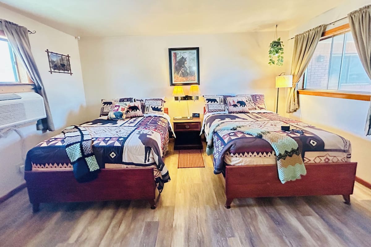 A room with two beds, each with patterned bedding, a framed picture on the wall, and a window with curtains.
