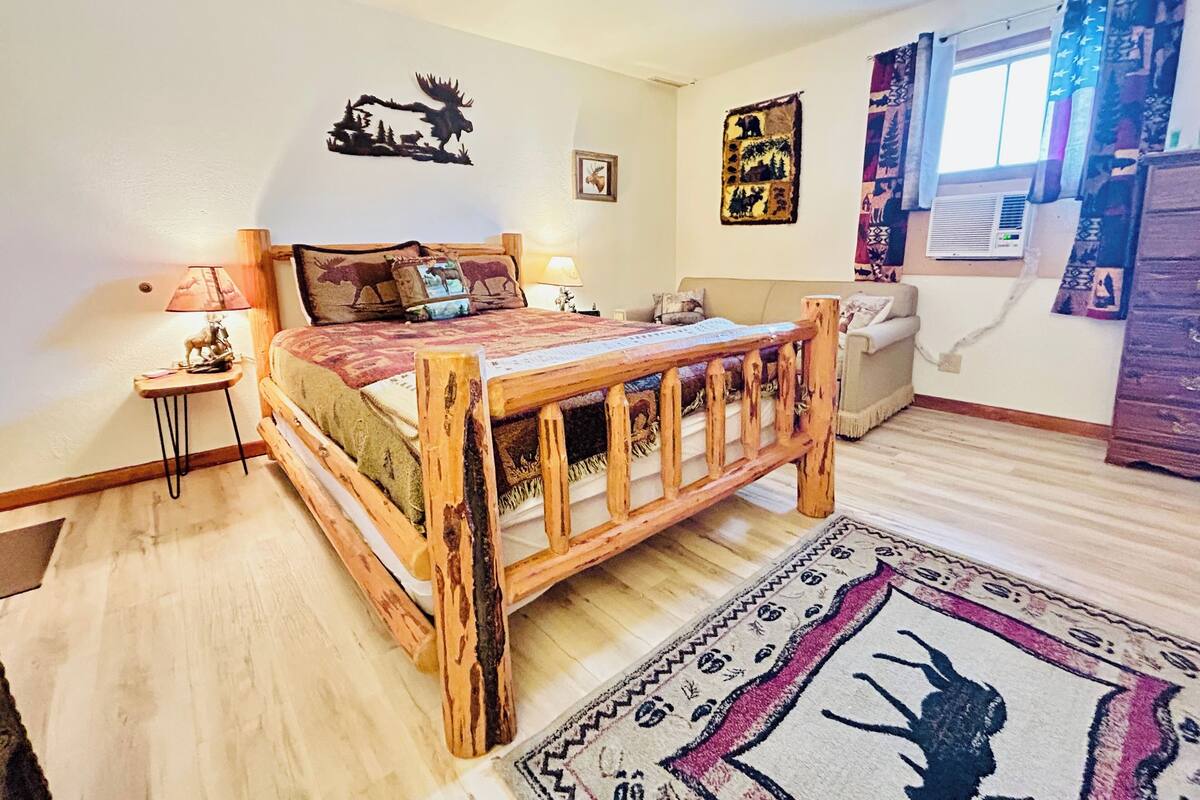 A cozy bedroom with a wooden bed, a small bedside table, a lamp, and a decorative moose wall art.
