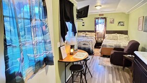 A compact room with a bed, a desk with a chair, a TV mounted on the wall, and a window with curtains. - The Lodge at Ute Lake (Logan)