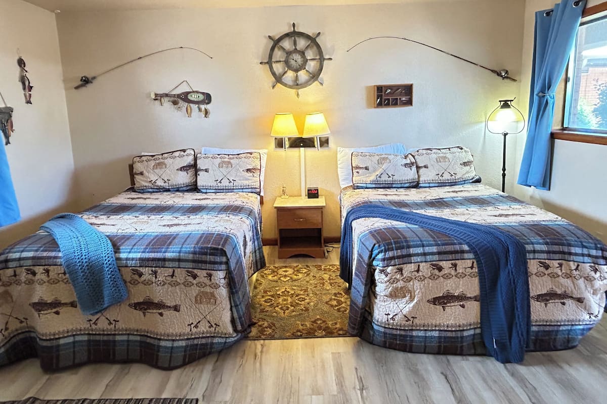 A double room with two beds, a ship's wheel decoration, a small table with lamps, and a window with curtains.