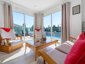 Amplia sala de estar con una mesa de vidrio, dos sillones y un sofá. Un gran ventanal ofrece vistas a una piscina y un área de estar exterior.