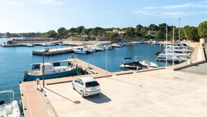 Un puerto deportivo con barcos amarrados, un coche y vistas del entorno, incluyendo edificios y árboles.