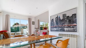 Un comedor con una mesa de vidrio, sillas anaranjadas y un cuadro de un paisaje urbano en la pared.
