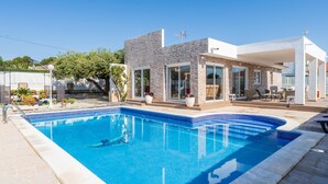 Una casa moderna con piscina, fachada de piedra y un patio cubierto.