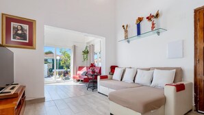 Una sala de estar con un sofá beige, un sofá rojo, un televisor y una repisa de vidrio con adornos.