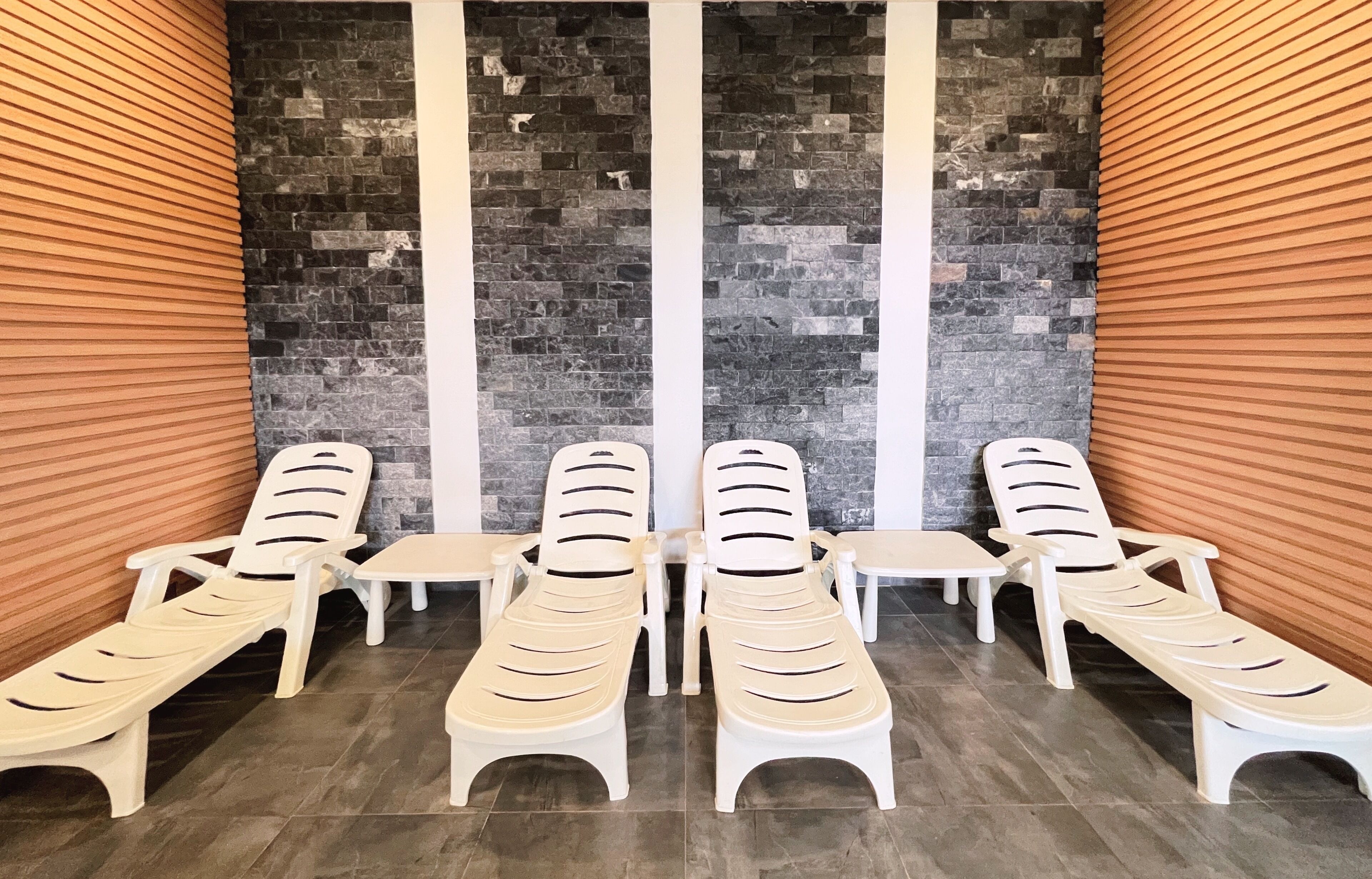 Een wellnessruimte met witte lounge fauteuils en een achtergrond van een stenen muur.