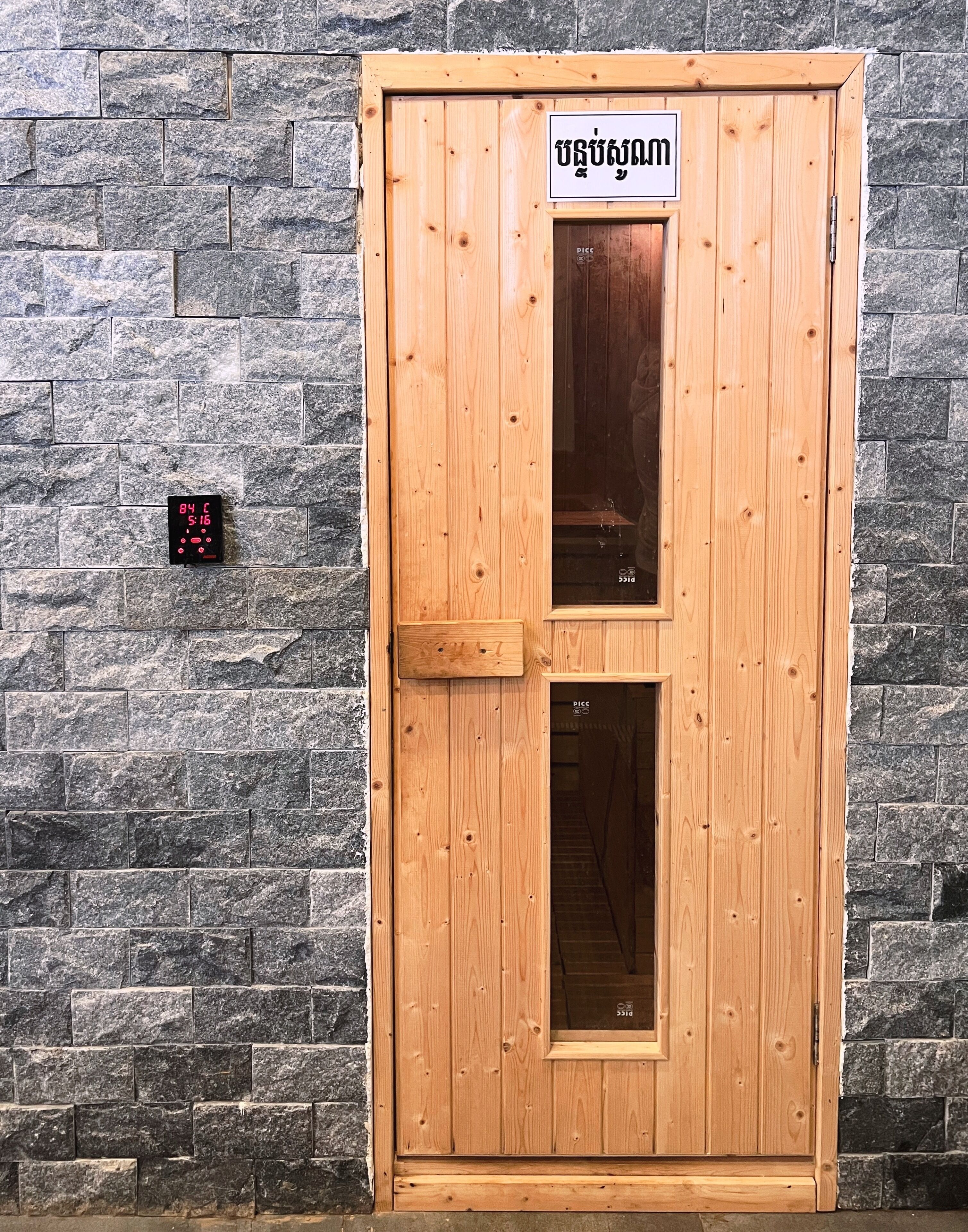 Una puerta de madera con un letrero encima, frente a una pared de piedra.