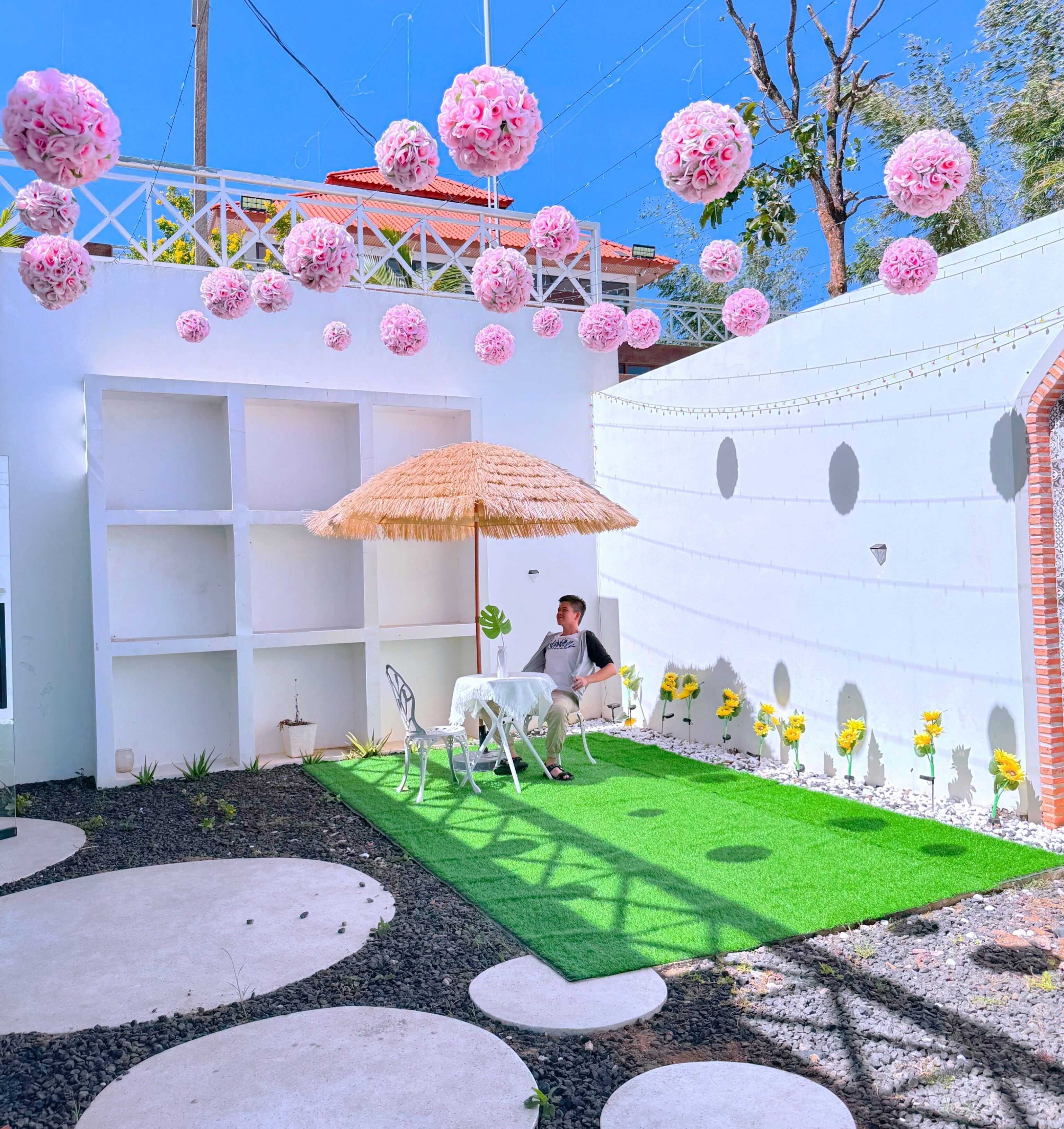 A patio area with a white wall, a thatched umbrella, a table, and chairs.