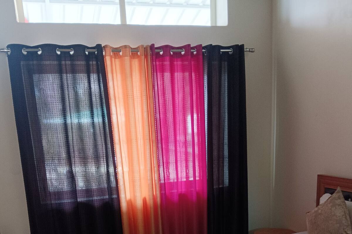 A bedroom with a bed, wooden floor, and a window with multi-colored curtains.