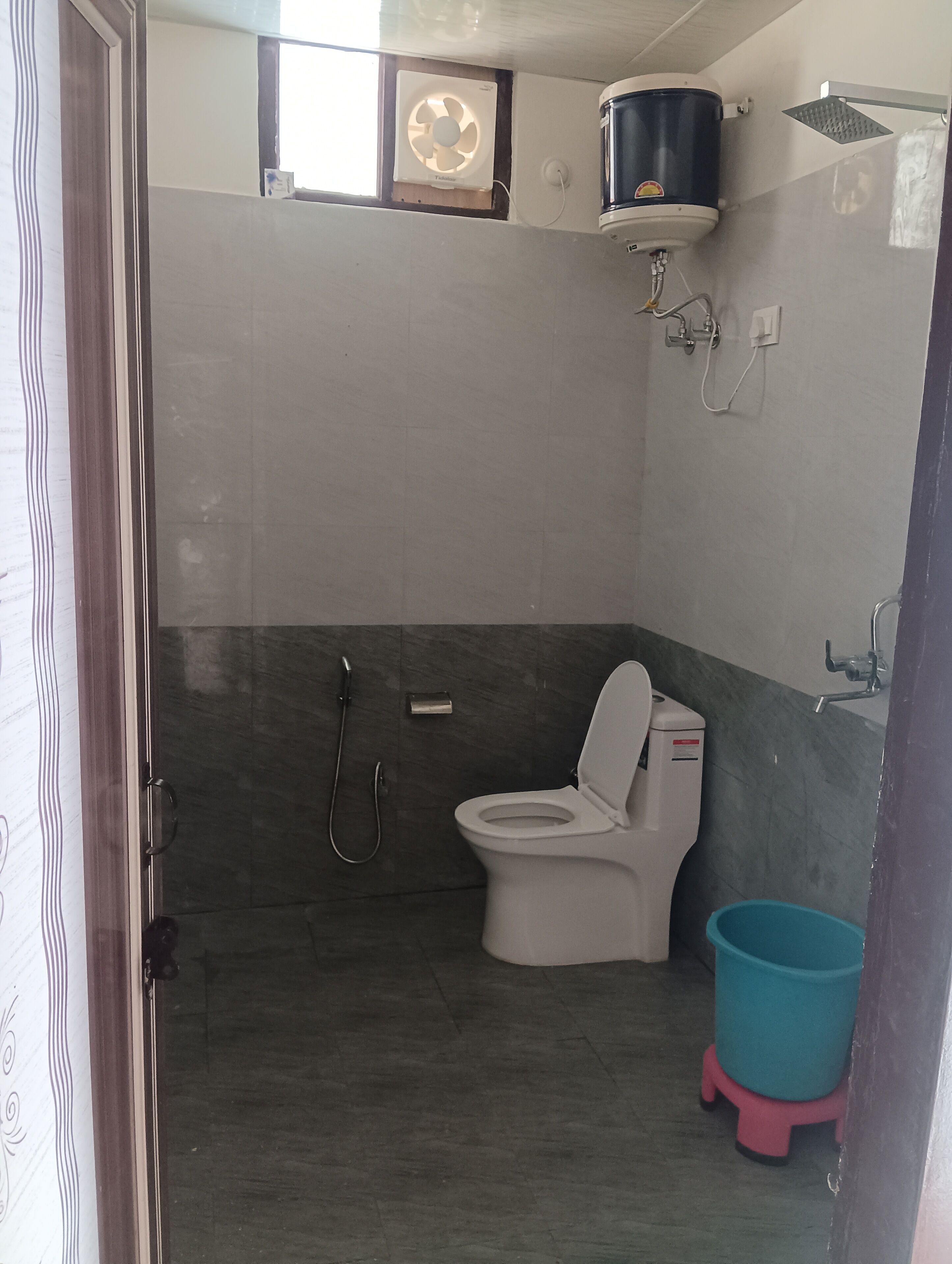 A bathroom with a toilet, a shower, and a blue bucket.