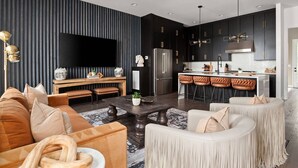 A modern living room with a sofa, coffee table, and a TV mounted on a wall with vertical lines. - Howdy Honey! 8 Beds ~ Hot Tub with Double Deck Rooftop & Amazing City Views  ~ 3 Miles to Broadway! (Nashville)