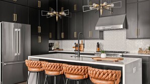 A modern kitchen with dark cabinetry, stainless steel appliances, and a central island with bar stools. - Howdy Honey! 8 Beds ~ Hot Tub with Double Deck Rooftop & Amazing City Views  ~ 3 Miles to Broadway! (Nashville)