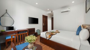 Ein Hotelzimmer mit einem Bett, einem Schreibtisch mit einem Laptop, einem Stuhl, einem kleinen Tisch mit Blumen und einem an der Wand befestigten Fernseher.