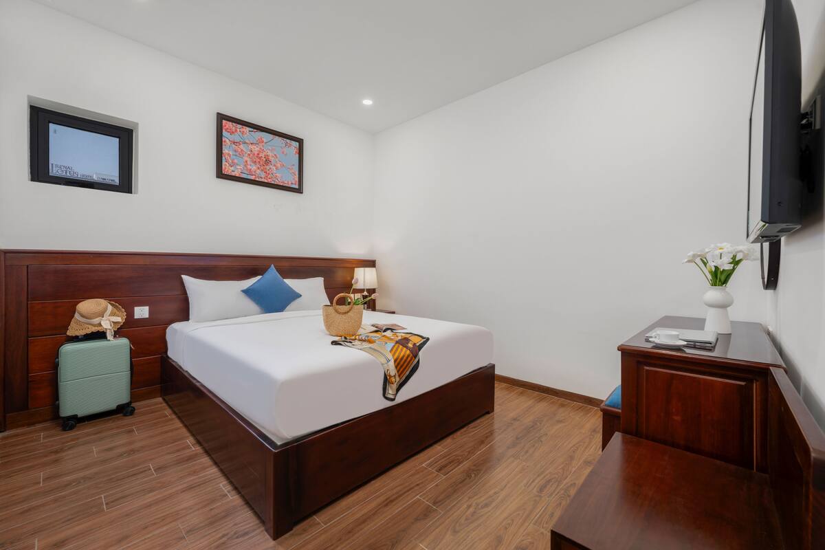 Habitación de hotel con una cama de madera, una mesita de noche, un televisor montado en la pared y un cuadro enmarcado sobre la cama.