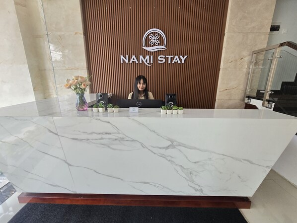 A reception desk at Nani Stay with a marble top, a wooden backdrop, and small potted plants. - Sea Near Me Hotel Danang (Da Nang)