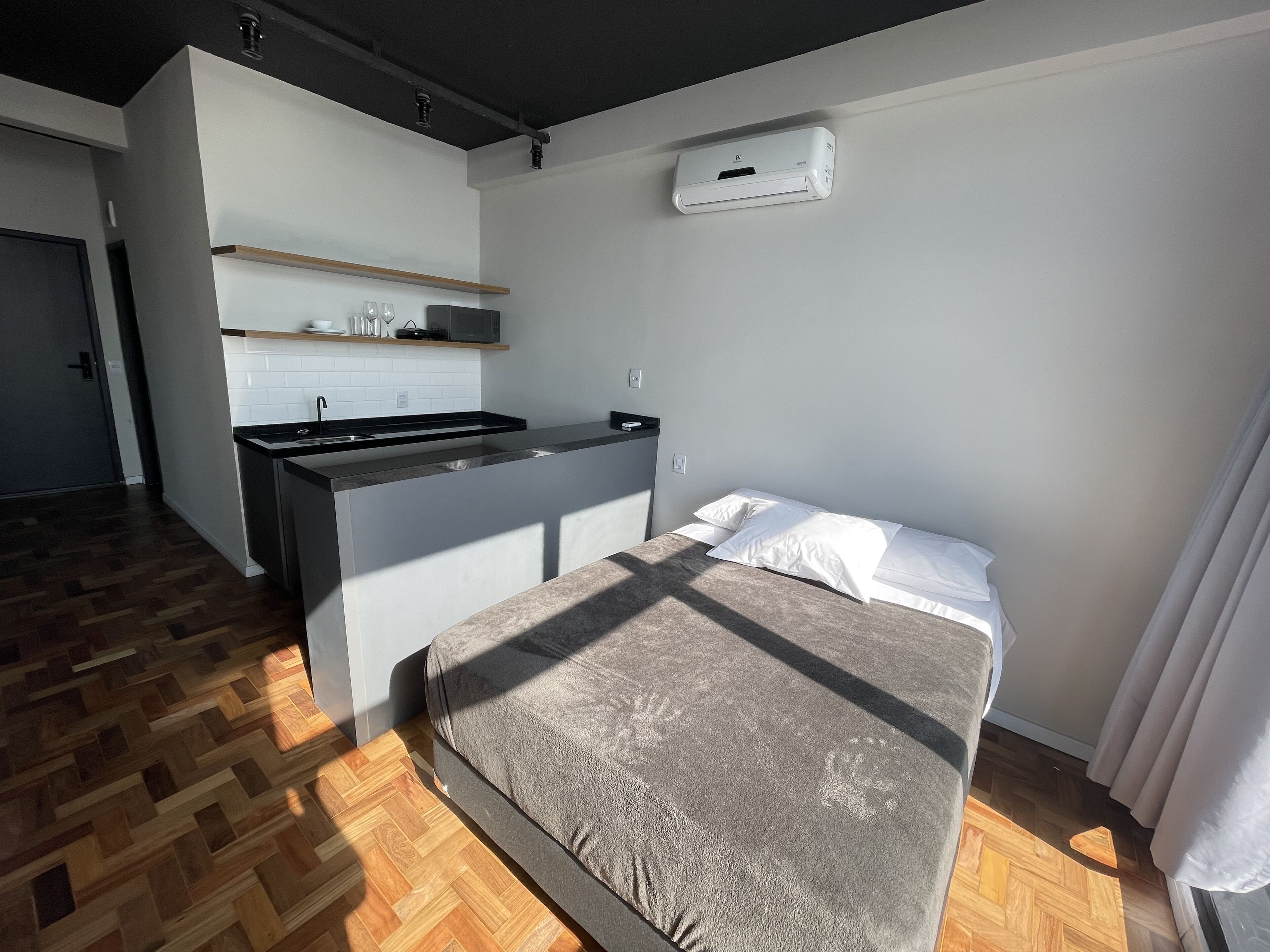 A compact room with a bed, a kitchenette, and a small bathroom.