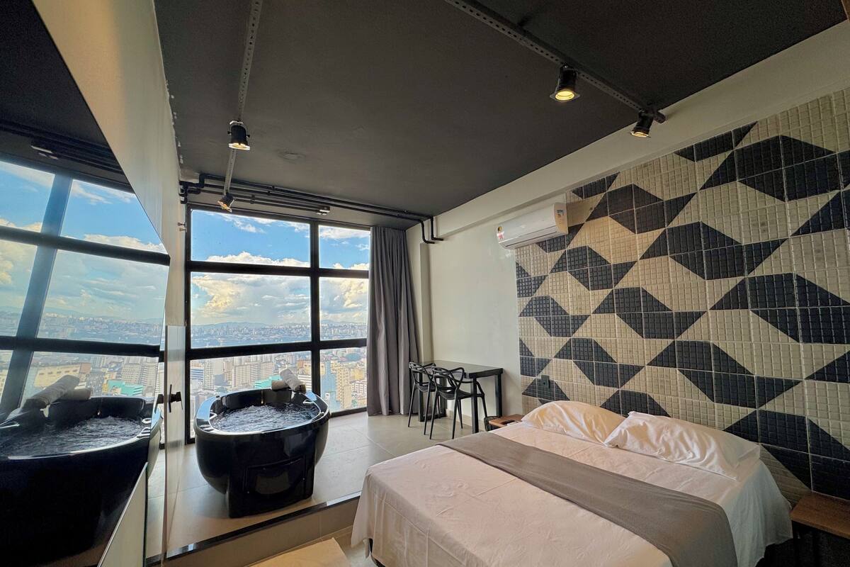 A hotel room with a large bed, a bathtub, a desk, and a view of the city.