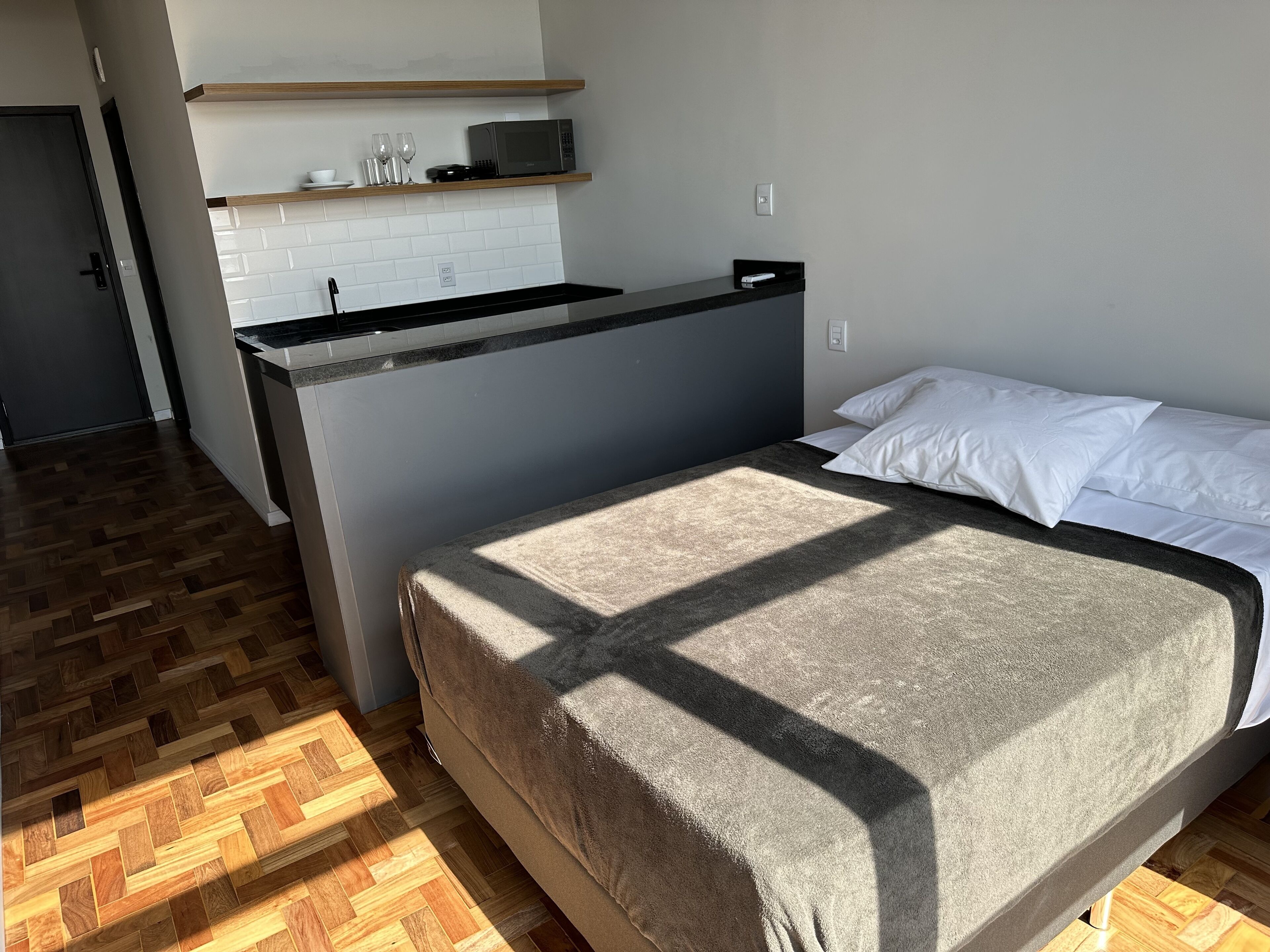 Un dormitorio con cama, una pequeña kitchenette y piso de madera.