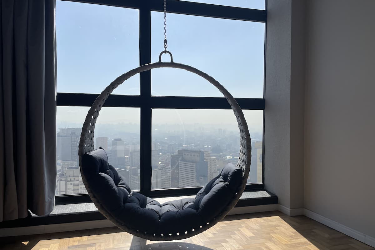 A hanging chair in a room with large windows overlooking a cityscape.