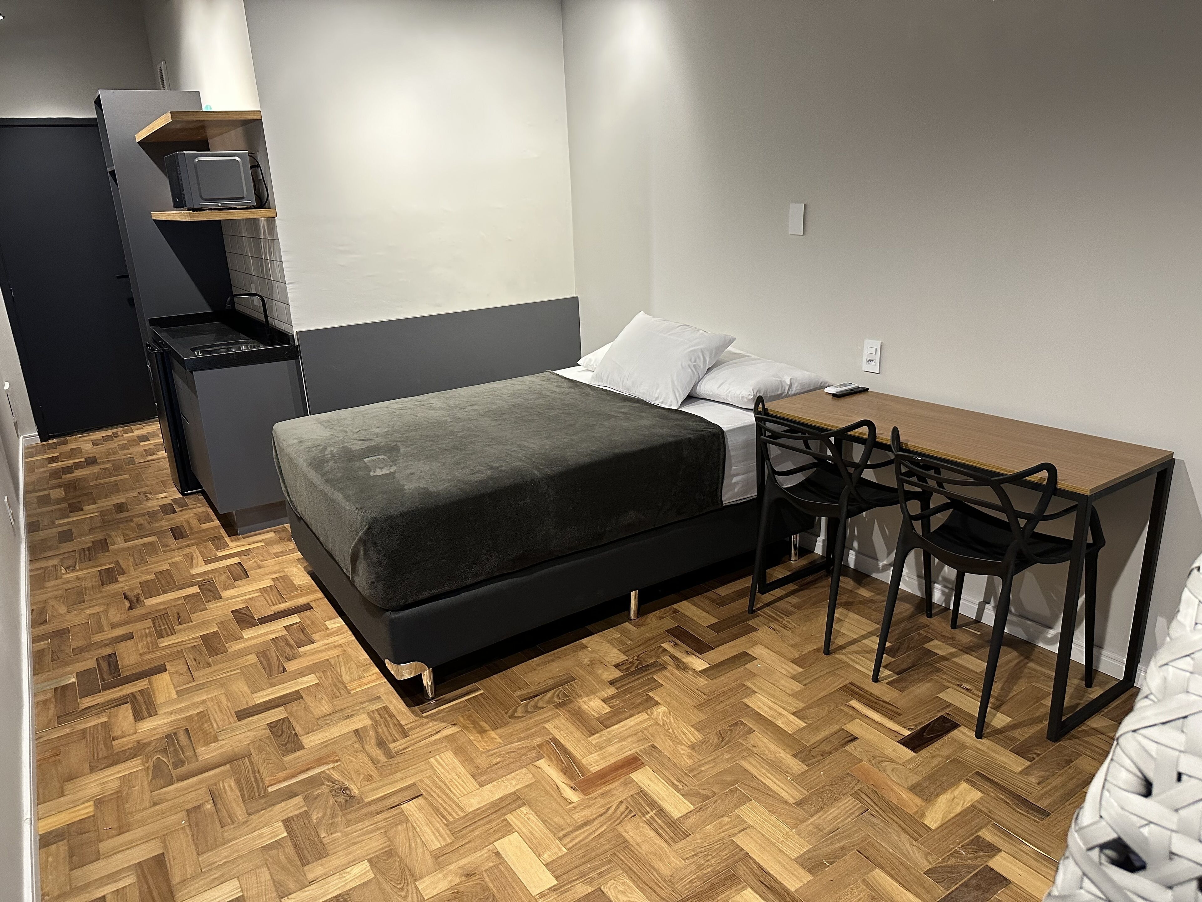 A compact bedroom with a bed, bedside table, and a small desk with a chair.