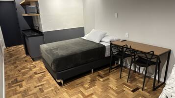 A compact bedroom with a bed, bedside table, and a small desk with a chair.