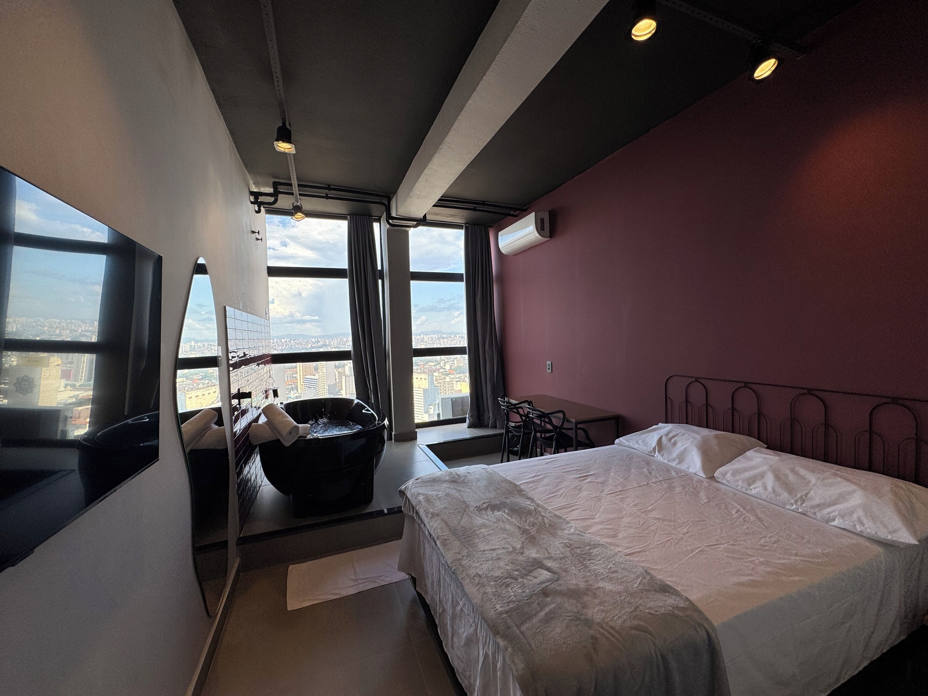 A modern hotel room with a large bed, a bathtub, a desk, and a view of the city.