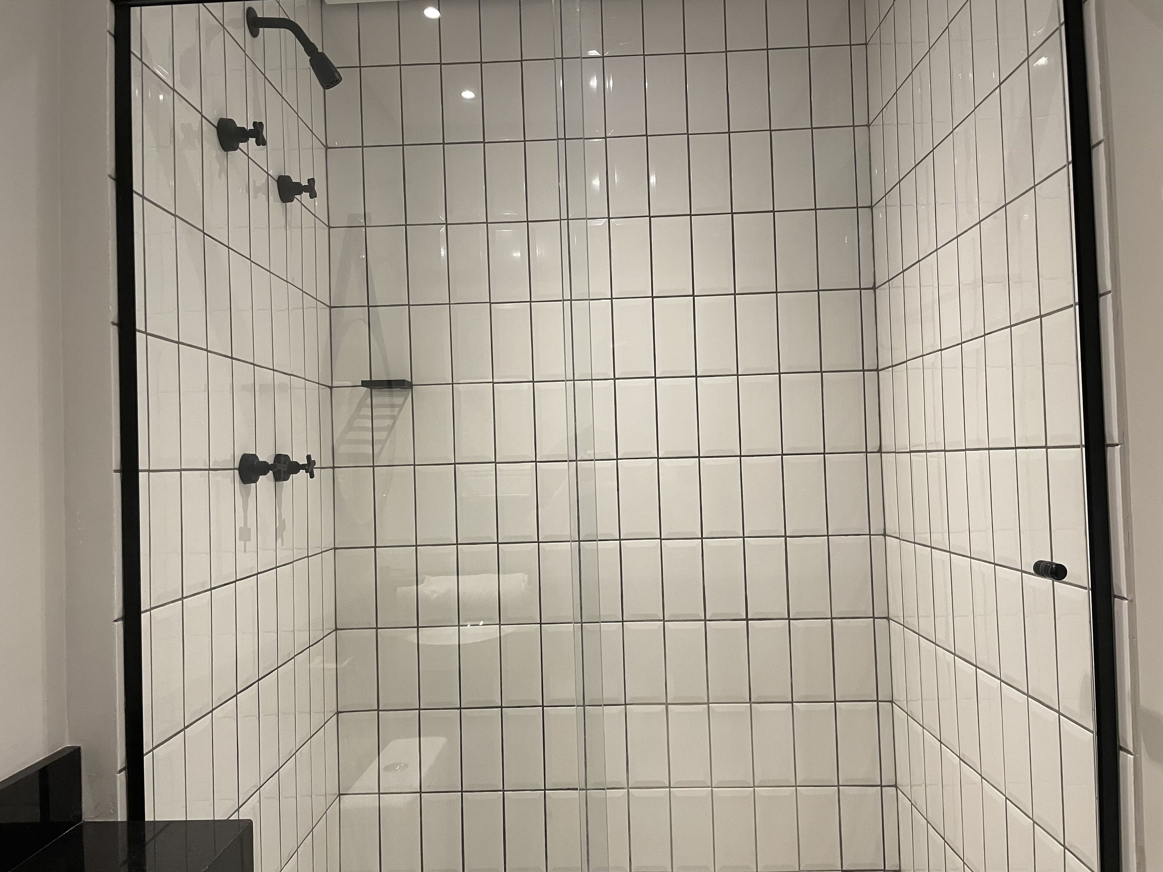 A modern shower with white tiles and black fixtures.