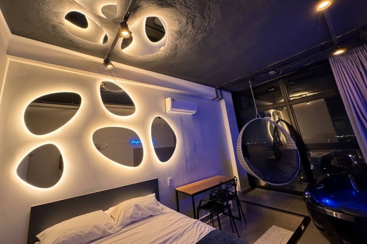 A modern hotel room with a unique ceiling design, a hanging chair, and a view of the city.