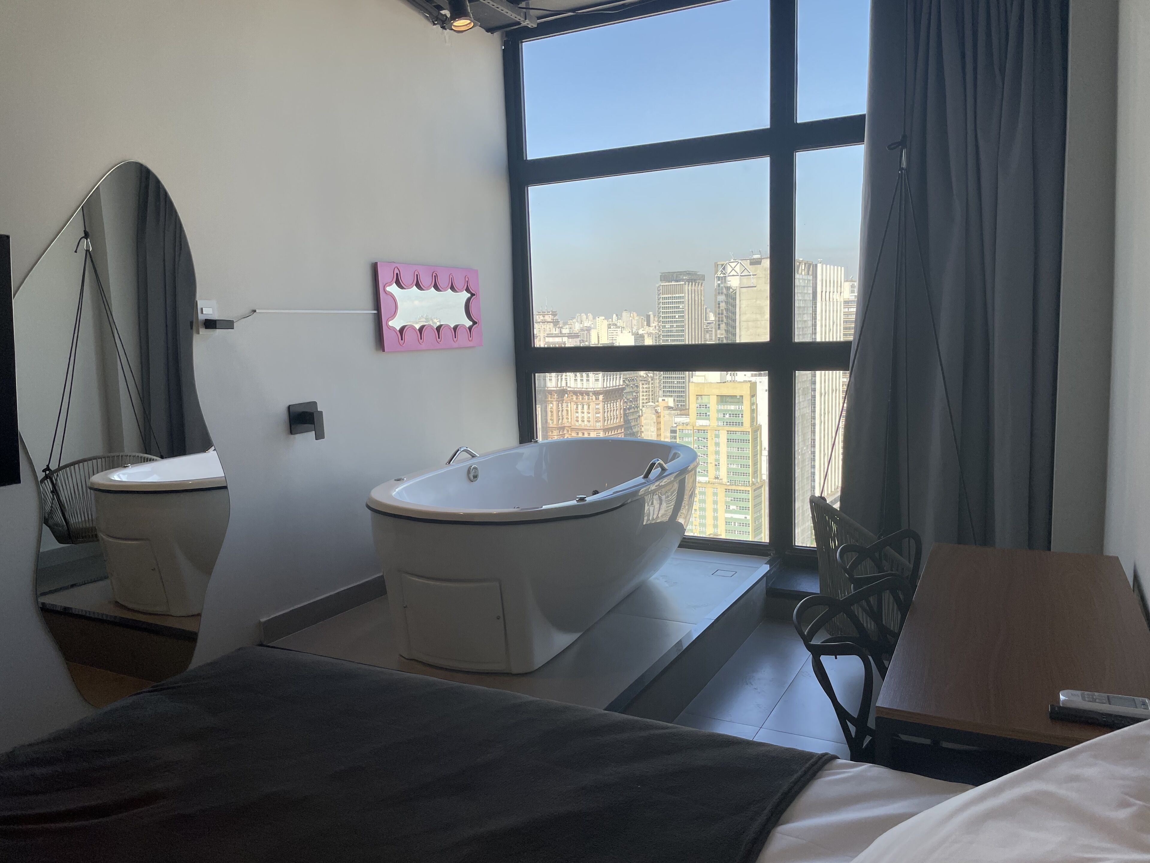 A modern bathroom with a bathtub, a toilet, and a large window offering a city view.
