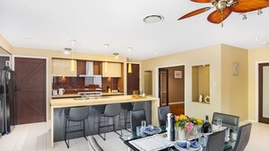 A modern kitchen with a central island, dining area with a glass table, and a ceiling fan. - Stylish 2BR House for a Memorable Stay @Stretton (Stretton)