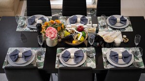 Mesa de comedor dispuesta para seis personas, con un frutero central, copas de vino y servilletas dobladas con cuidado.