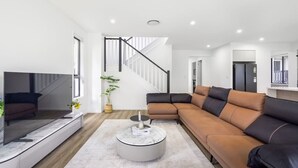 Uma sala de estar moderna com um sofá seccional, uma televisão de tela plana, uma mesa de centro redonda e uma escada.