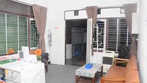 A room with a desk, a sofa, a small table, an air conditioner, and a window with curtains. - DE HOMESTAY BANJARMASIN (Banjarmasin)