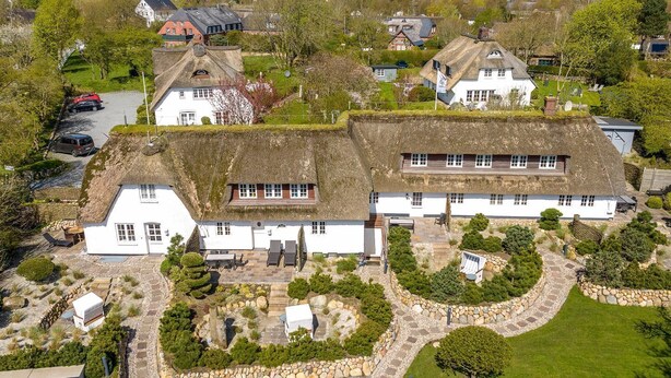 A traditional white house with a thatched roof, surrounded by a well-maintained garden with stone pathways and various plants.