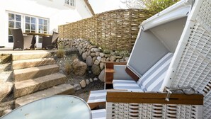 A cozy outdoor seating area with wicker furniture, a stone wall, and a view of a white building.