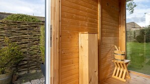 A wooden cabin with a large window, a wooden door, and a small wooden stool.