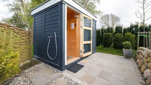 A small, dark blue outdoor sauna with a wooden door and a shower hose attached to the wall.